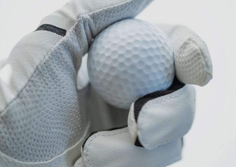 a hand wearing a white golf glove holding a golf ball