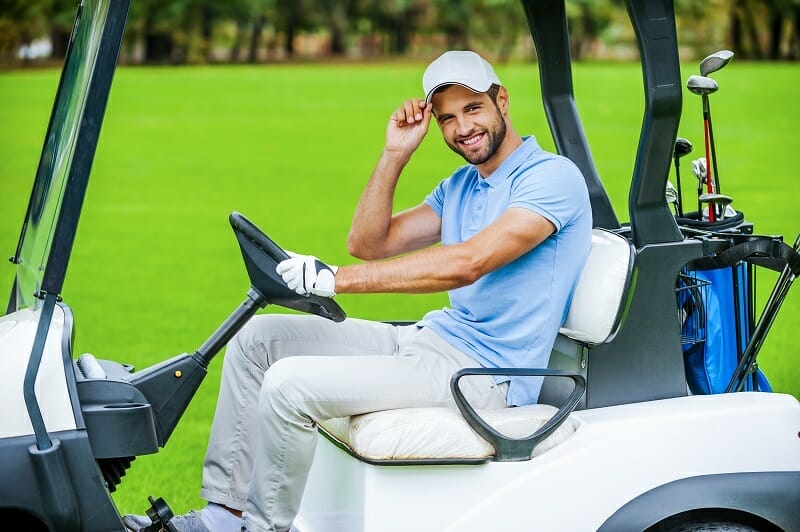 Man driving golf cart. Side view of handsome young man driving a golf cart and looking at camera